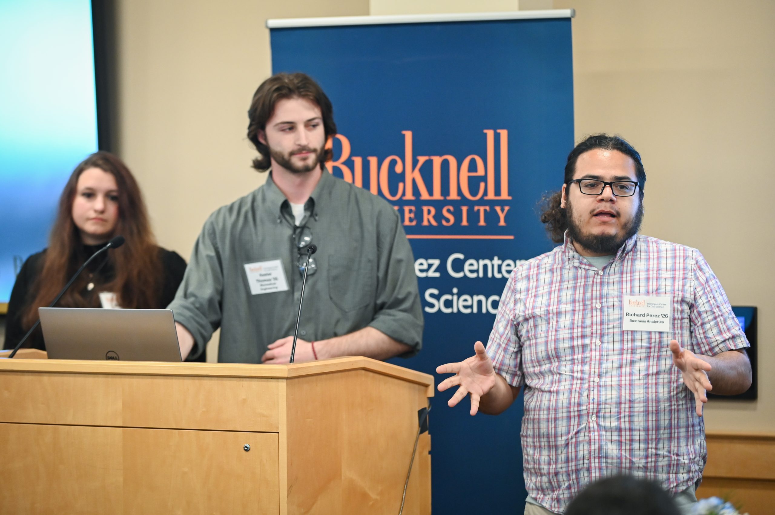 Claire Engel and Gwen Radecki standing behind a podium next to a screen that reads, "Acomplishments."