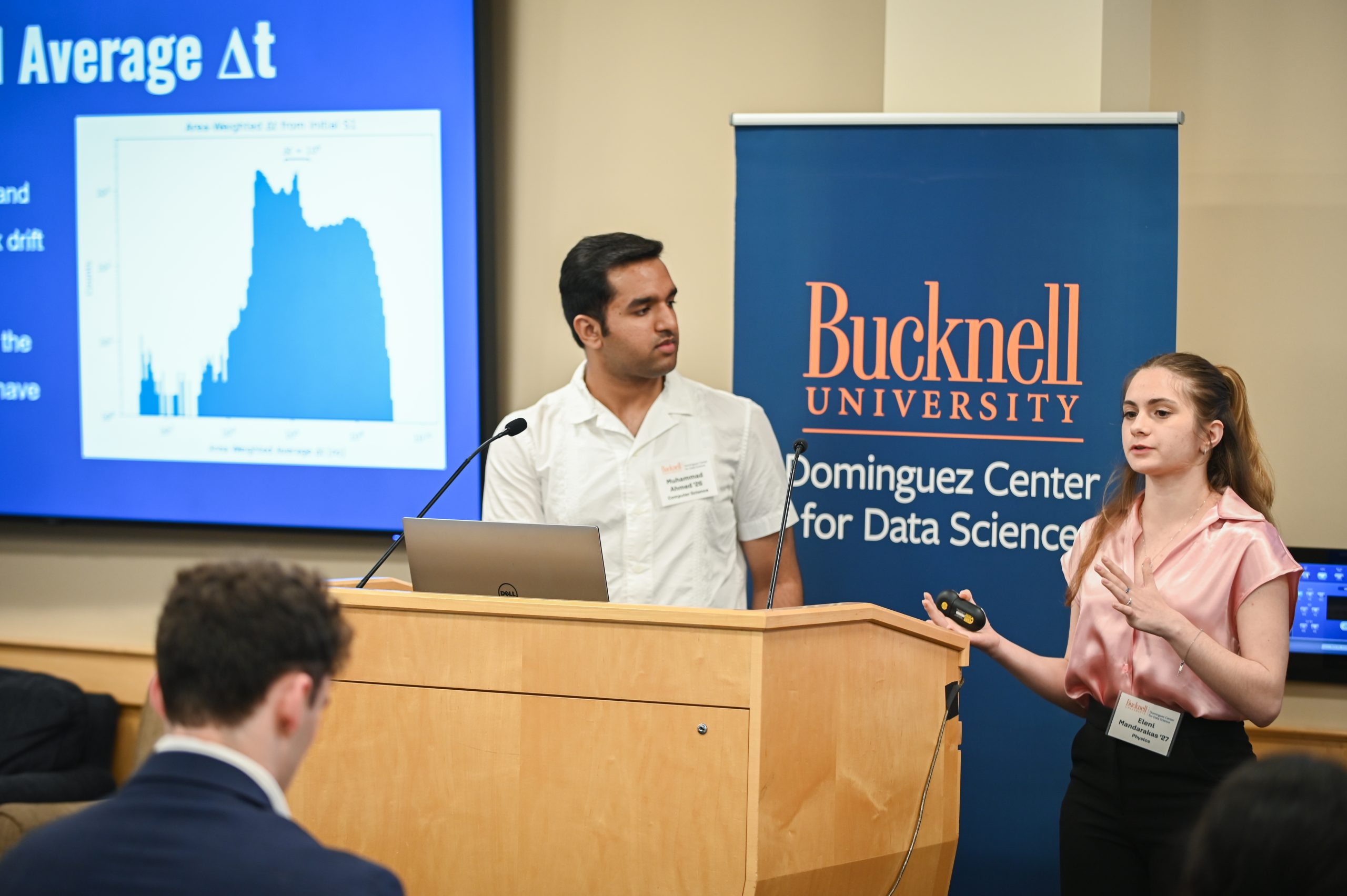 Claire Engel and Gwen Radecki standing behind a podium next to a screen that reads, "Acomplishments."