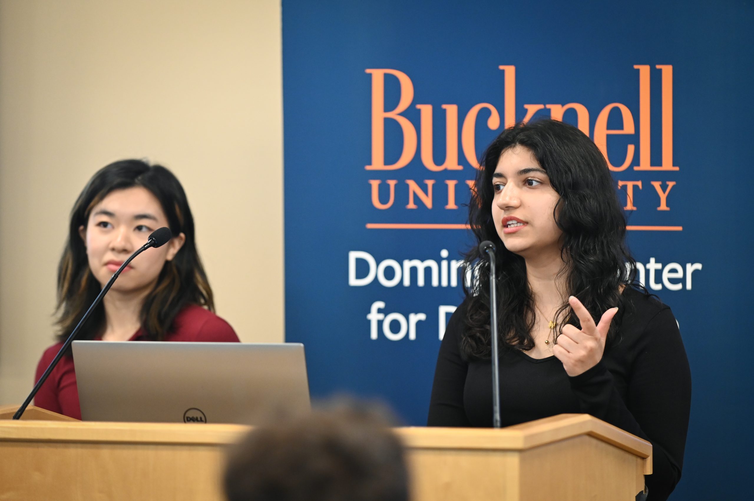 Claire Engel and Gwen Radecki standing behind a podium next to a screen that reads, "Acomplishments."