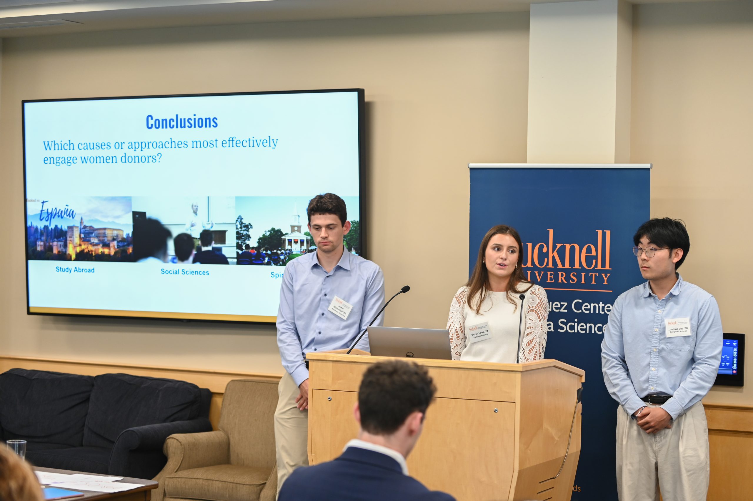 Claire Engel and Gwen Radecki standing behind a podium next to a screen that reads, "Acomplishments."