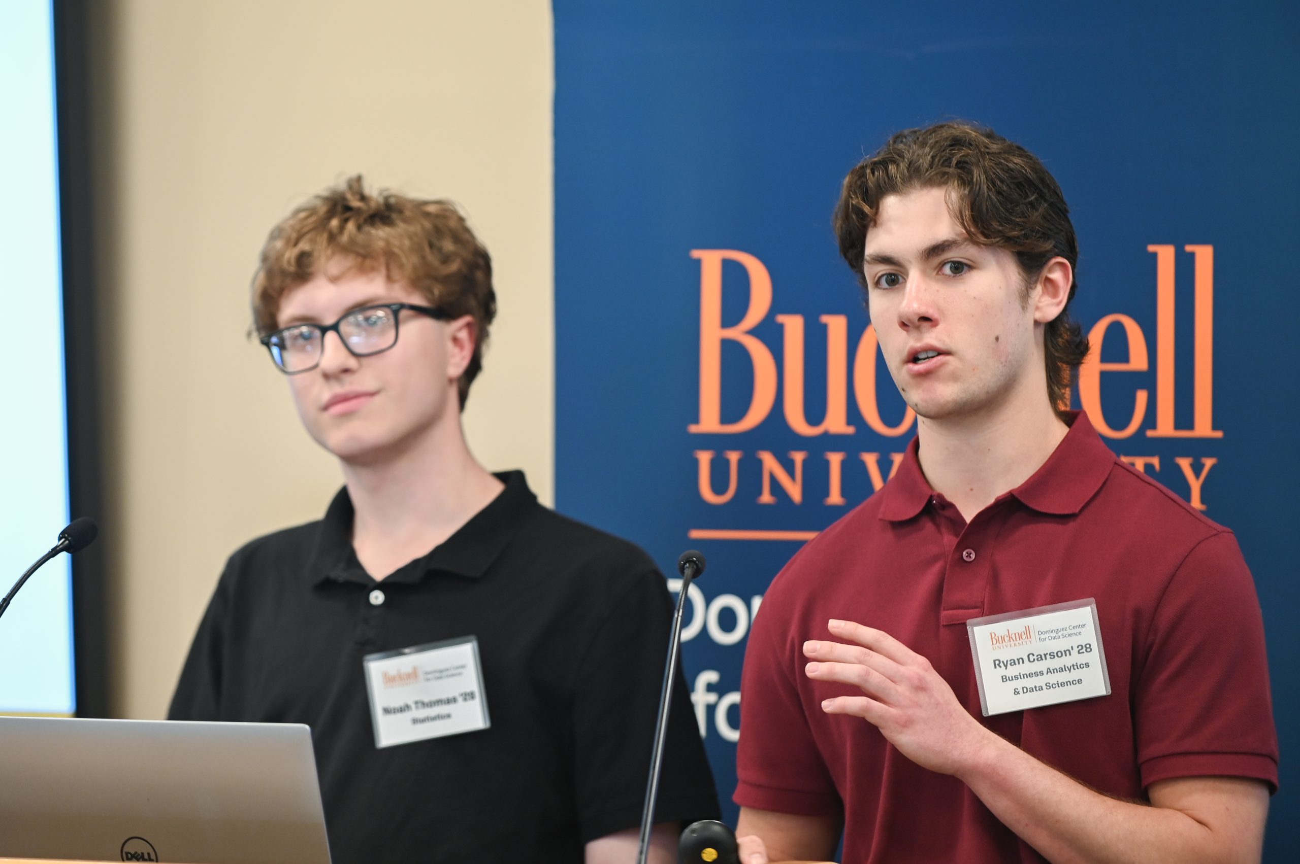Claire Engel and Gwen Radecki standing behind a podium next to a screen that reads, "Acomplishments."