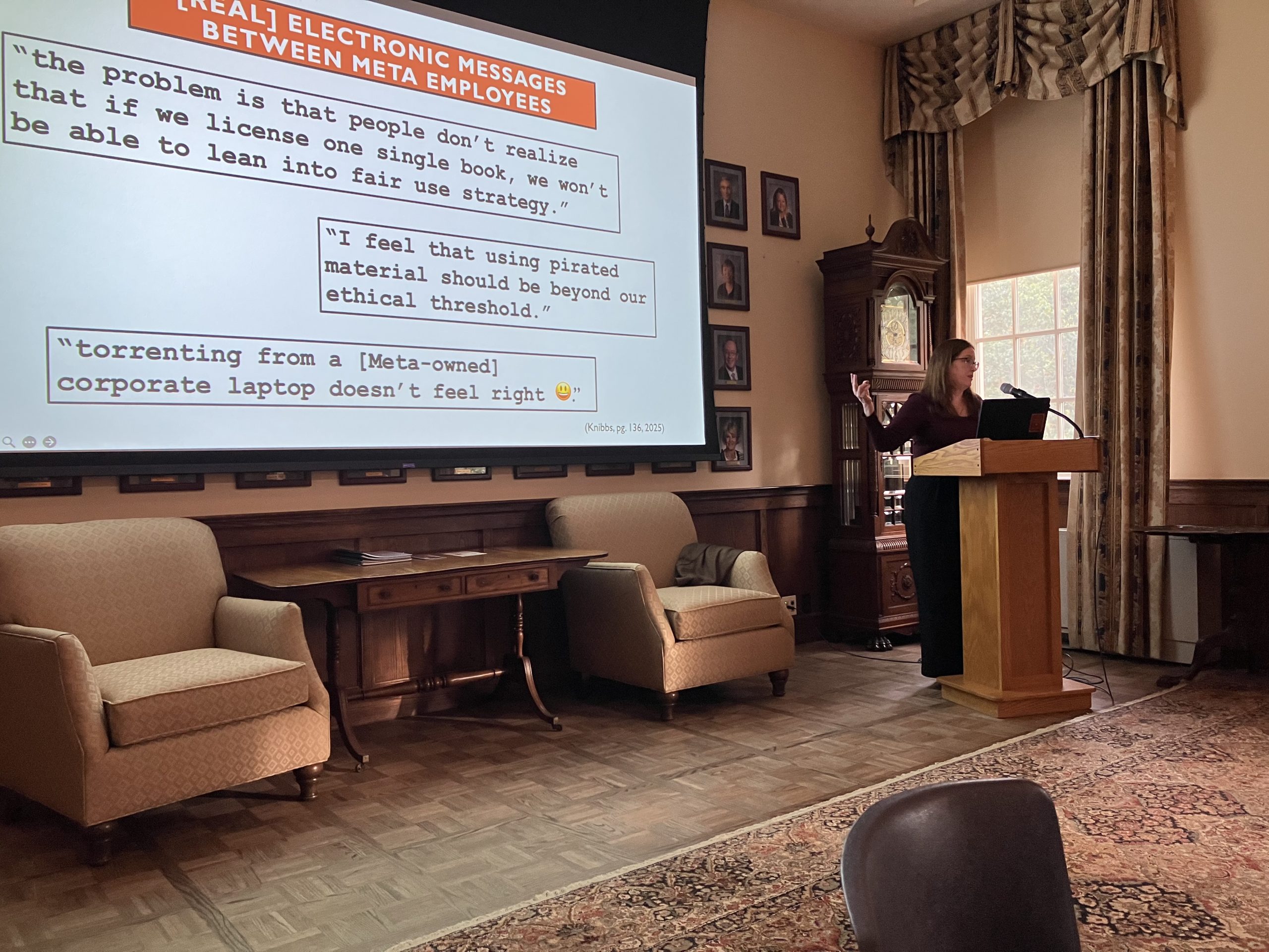 Rachel Sweeney standing at a podium, speaking and gesturing to a screen that reads, "[Real] electronic messages between meta employees."